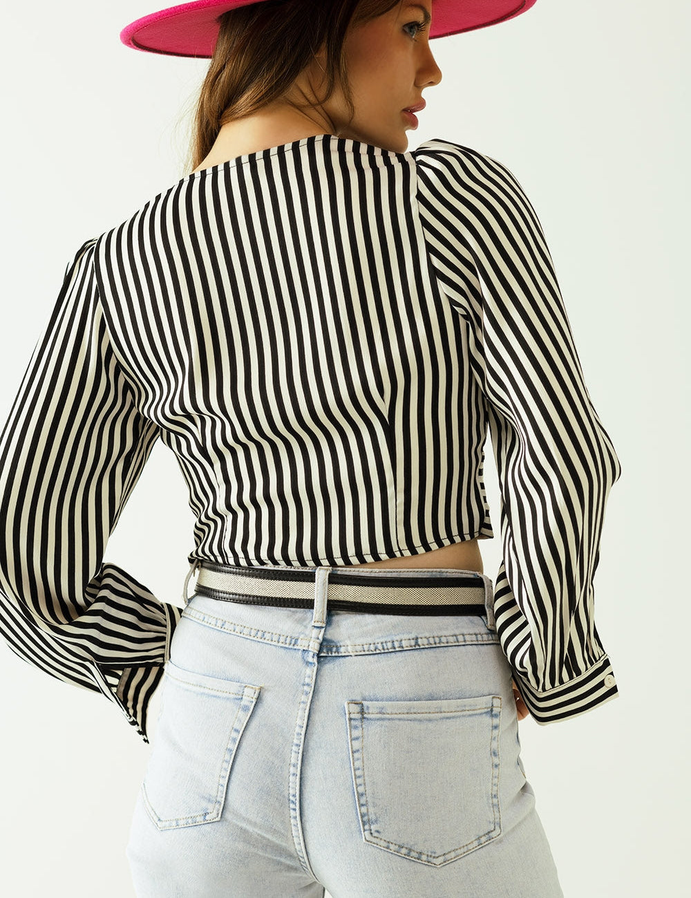 Woman wearing Nivarra Twisted Satin Crop Top with black-and-white stripes and pink hat, highlighting bold fashion statement.