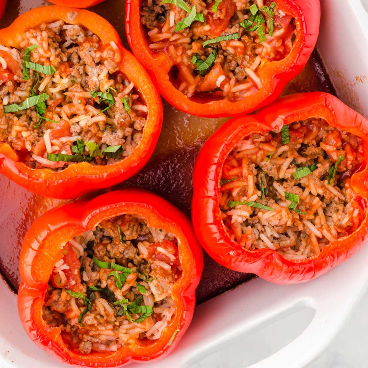 Homemade Ukrainian stuffed peppers with rice and meat filling, garnished with fresh herbs in a white baking dish.