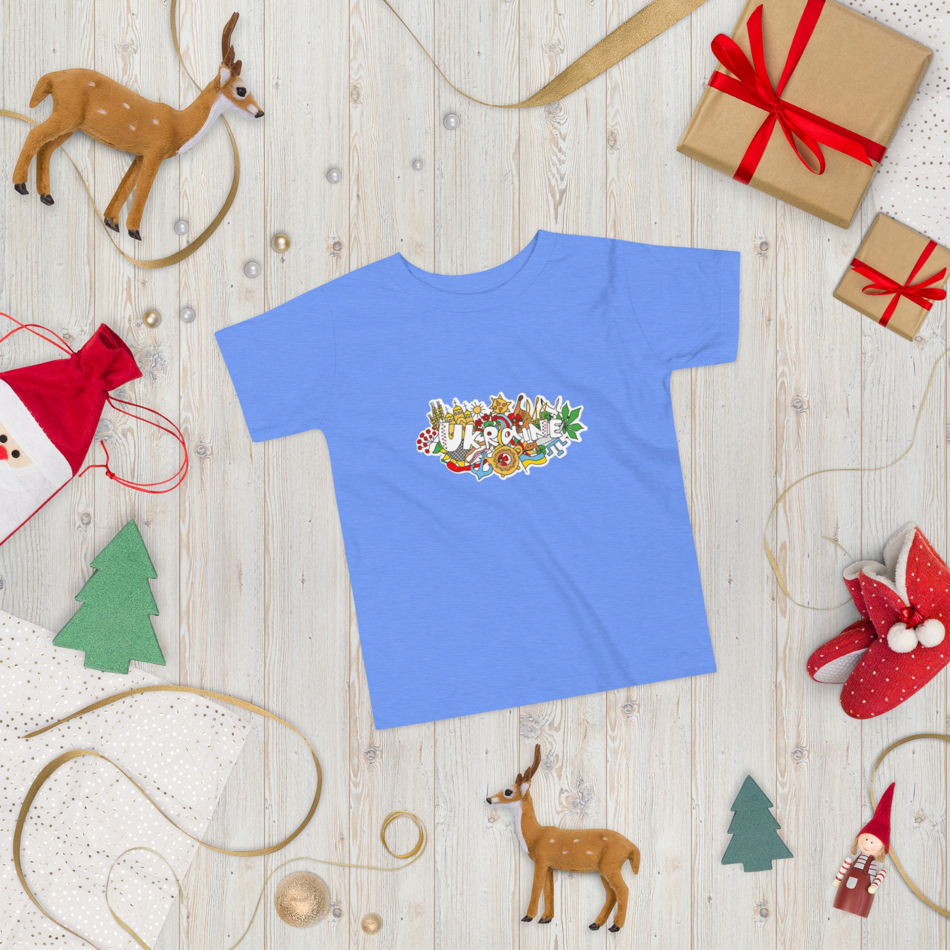 Toddler short sleeve T-shirt with colorful Ukraine design on wooden holiday-themed background with gifts and decorations.