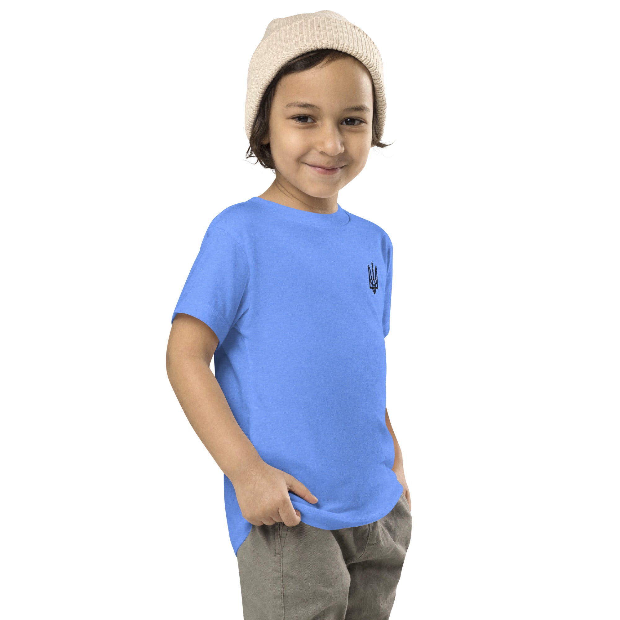 Toddler wearing blue short-sleeve tee with Ukrainian Tryzub print and beige beanie, smiling and posing with hands in pockets.
