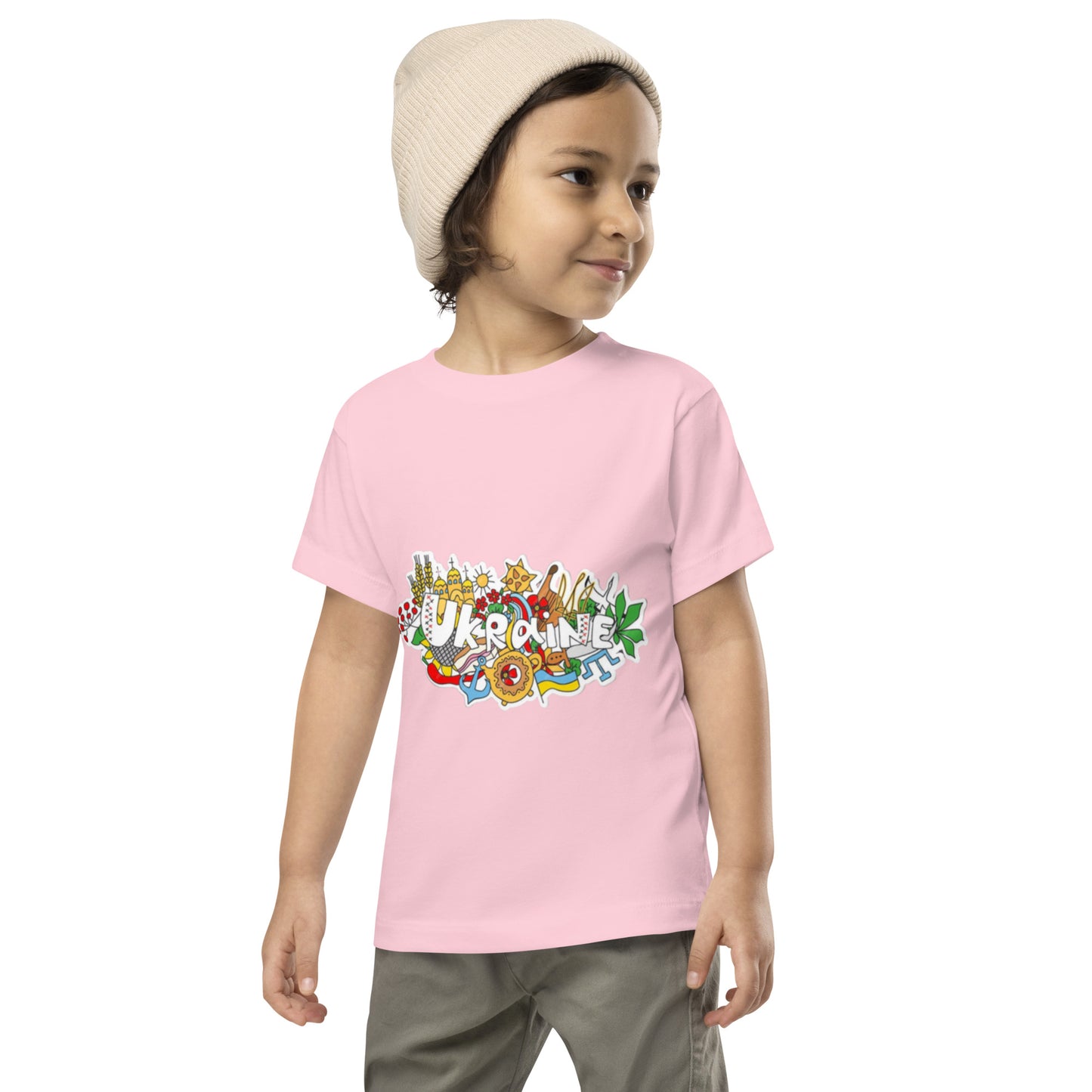 Toddler wearing pink short sleeve T-shirt with colorful Ukraine design, smiling and standing in casual outfit.