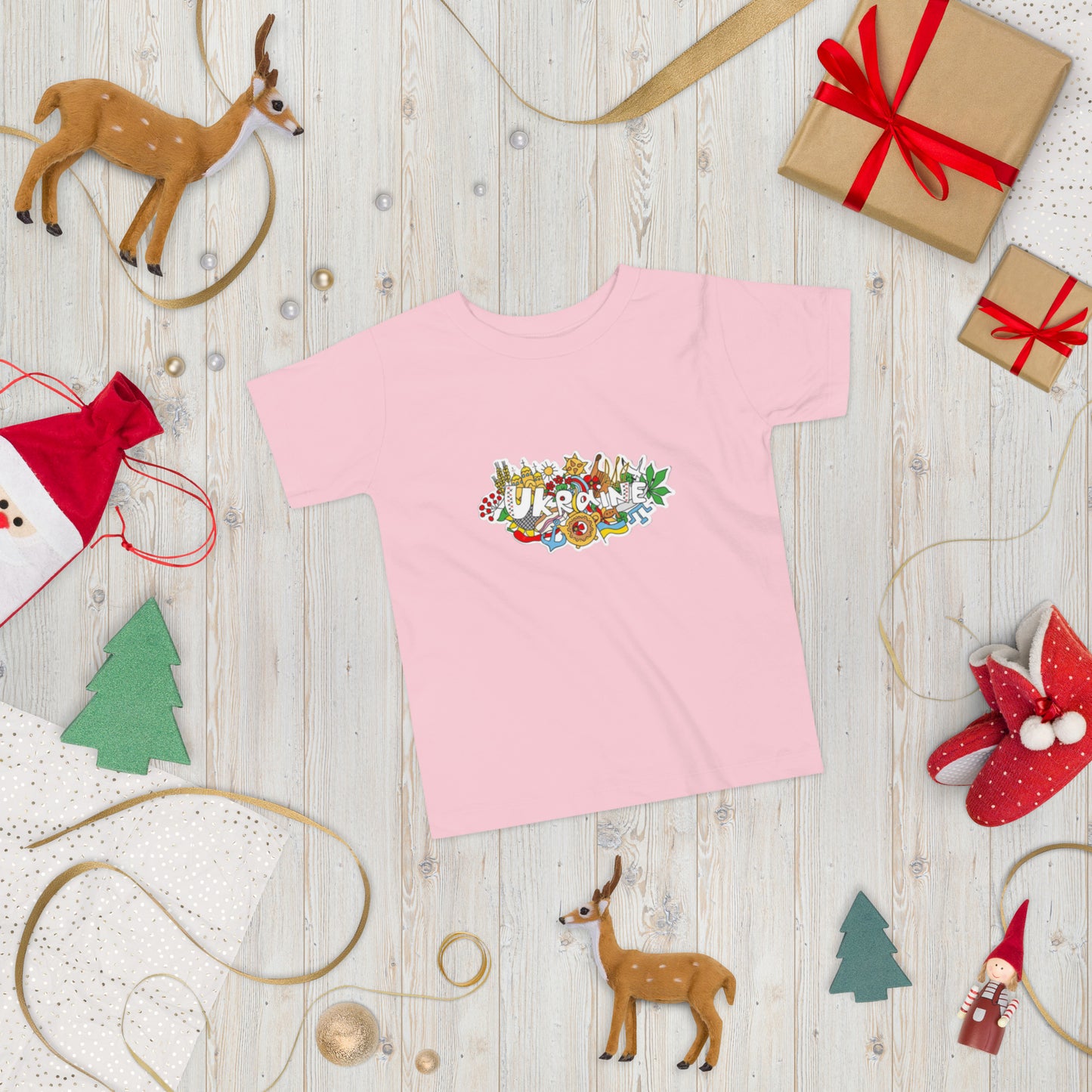 Pink toddler t-shirt with Ukraine design on festive holiday-themed background with gift boxes and toy reindeer.