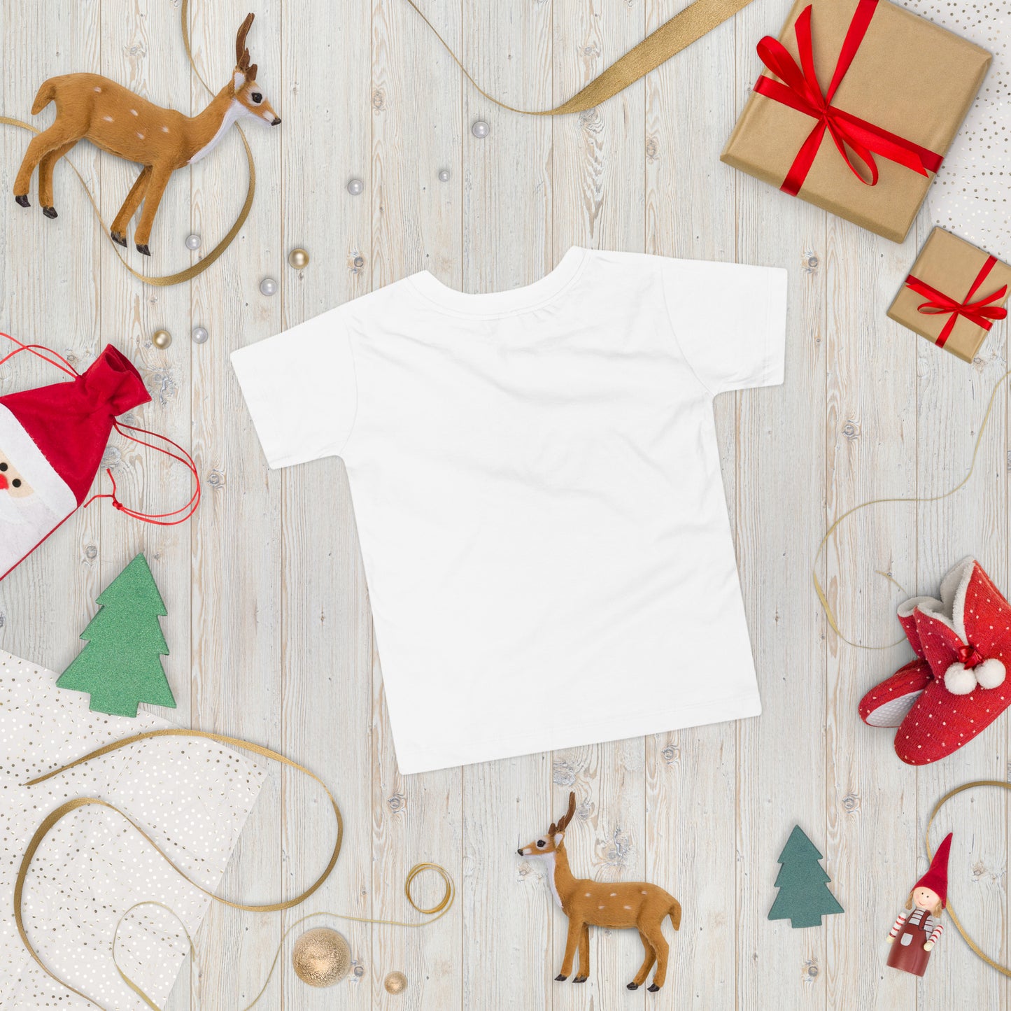 White toddler t-shirt on festive wooden background with holiday decorations including reindeer and gift boxes.