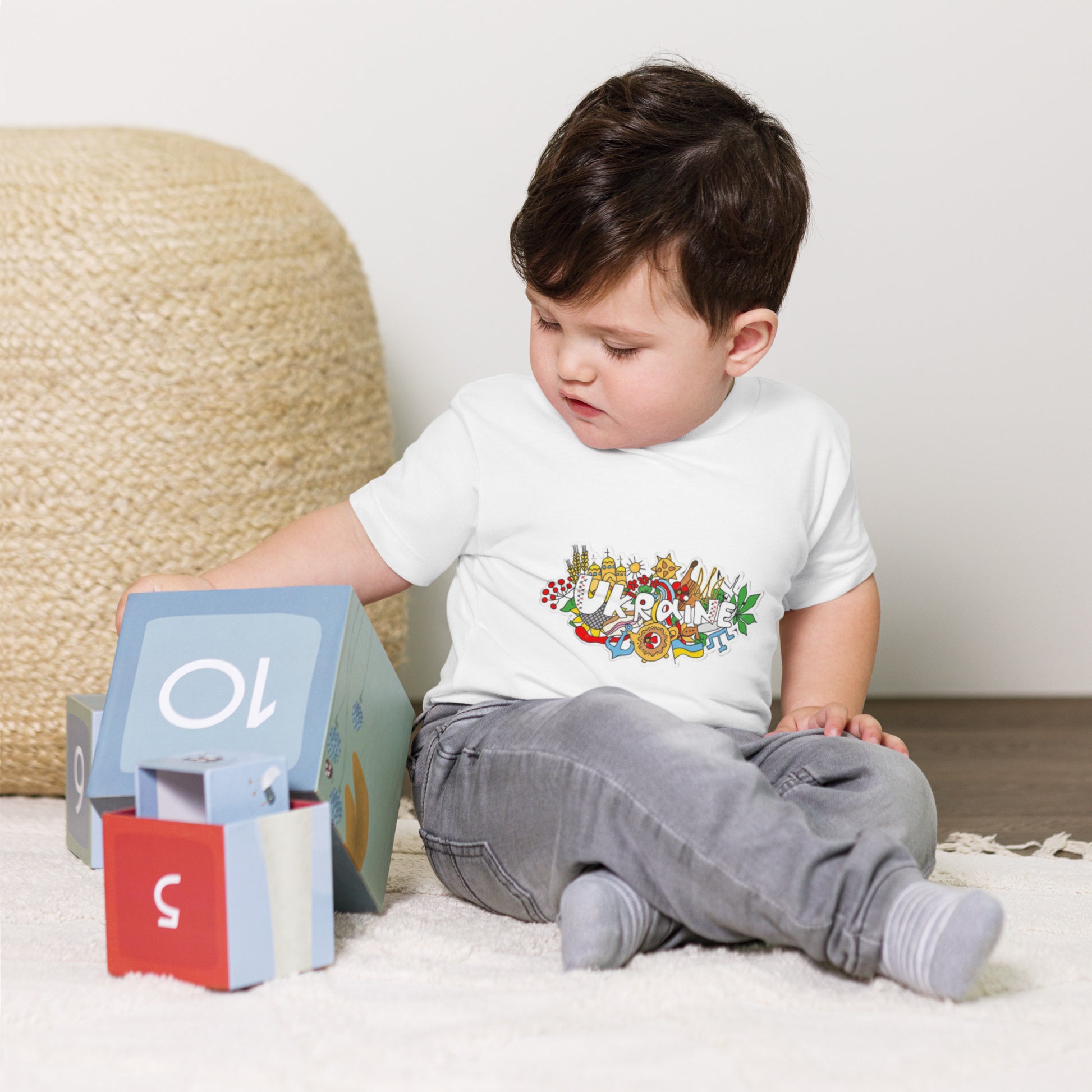 Toddler wearing Ukraine-themed short sleeve t-shirt plays with colorful blocks indoors.