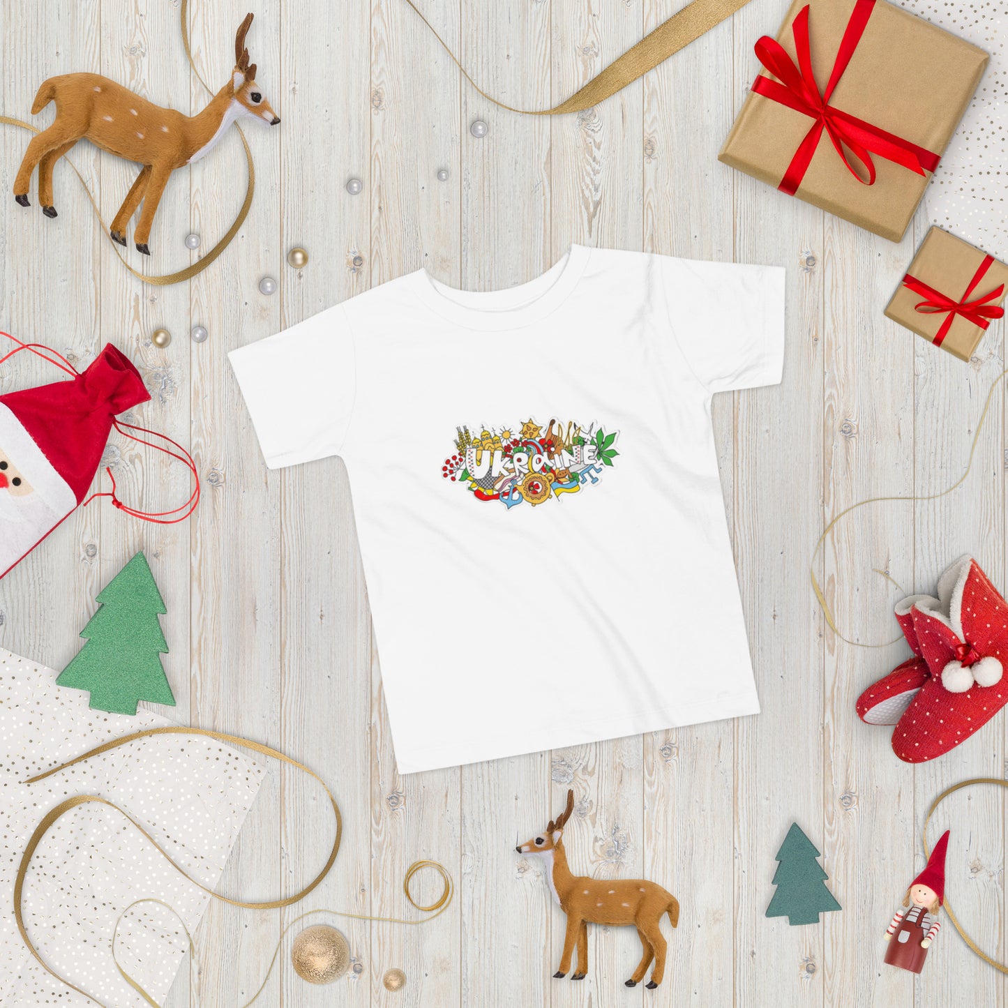 Toddler short sleeve T-shirt with Ukraine design, surrounded by holiday decorations and gifts on a wooden background.