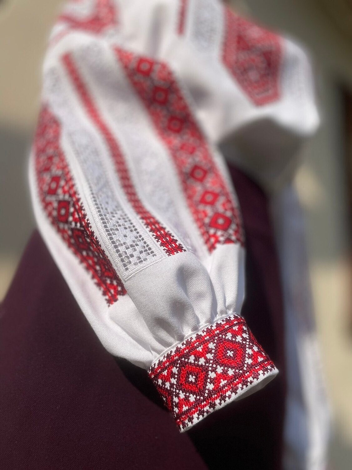 Close-up of a traditional Ukrainian vyshyvanka sleeve with red and black cross-stitch embroidery on cotton fabric.