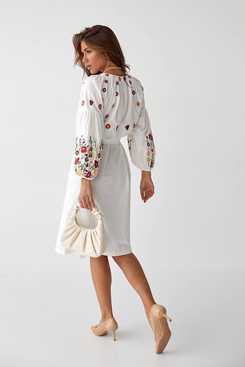 Woman wearing traditional Ukrainian embroidered dress with floral pattern, Vyshyvanka-style, holding a white purse.