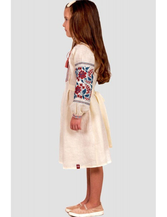 Girl wearing a traditional Ukrainian embroidered linen dress with floral cross-stitch and buttoned straps.