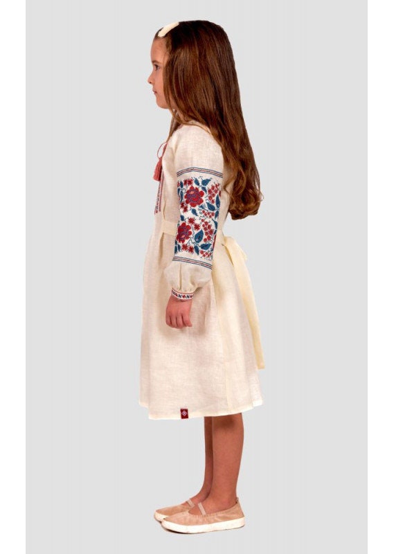 Girl wearing a traditional Ukrainian embroidered linen dress with floral cross-stitch and buttoned straps.