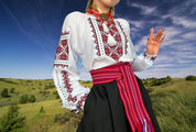 Woman wearing traditional Ukrainian embroidered Vyshyvanka blouse with red cross-stitch, standing in a grassy field.