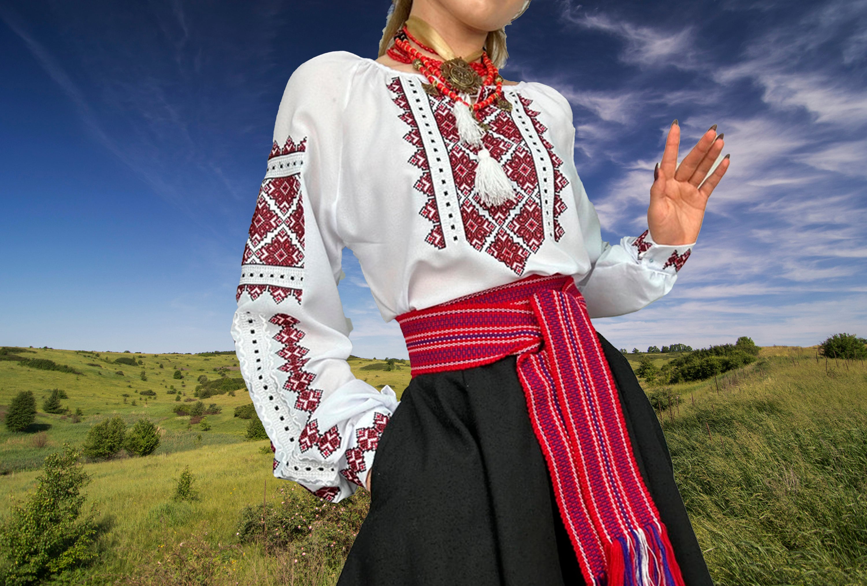 Woman wearing traditional Ukrainian embroidered Vyshyvanka blouse with red cross-stitch, standing in a grassy field.
