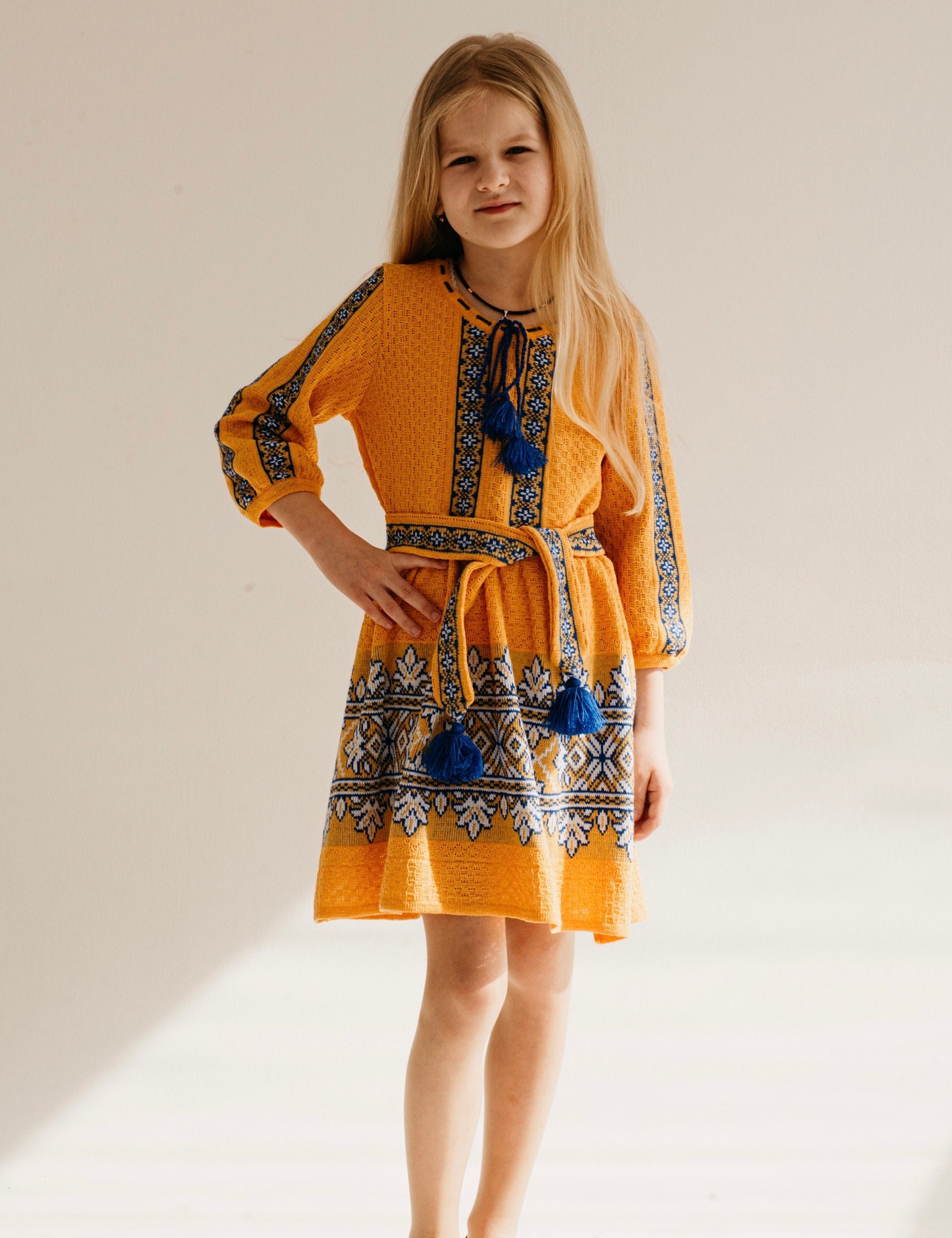 Girl wearing a traditional Ukrainian knitted dress in golden yellow with blue and white embroidery, perfect for festive occasions.