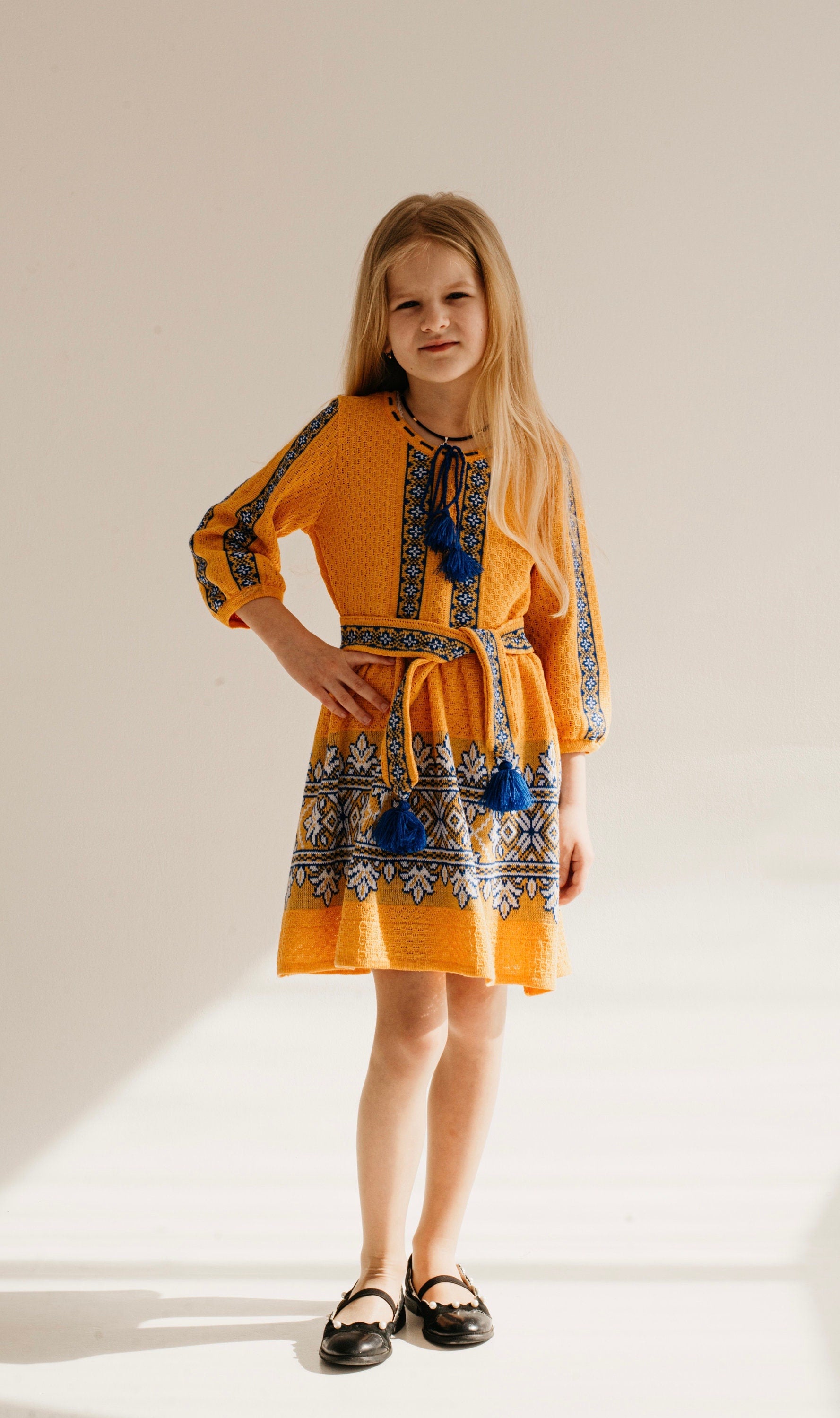 Girl wearing a traditional Ukrainian knitted dress in golden yellow with blue and white embroidery, perfect for festive occasions.