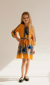 Girl wearing a traditional Ukrainian knitted dress in golden yellow with blue and white embroidery, perfect for festive occasions.