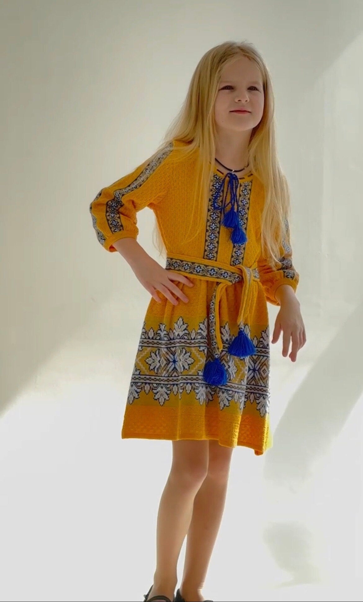 Girl wearing a golden Ukrainian knitted dress with blue and white embroidery, showcasing traditional and modern elegance.