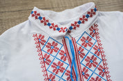 Ukrainian vyshyvanka for boys with red and blue embroidery, stand-up collar, and traditional ornamental design on white fabric.