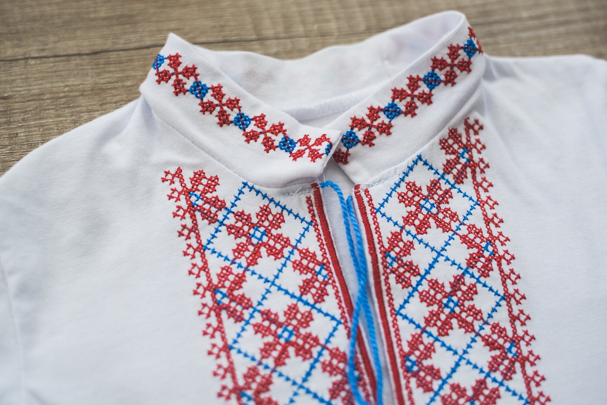 Ukrainian vyshyvanka for boys with red and blue embroidery, stand-up collar, and traditional ornamental design on white fabric.