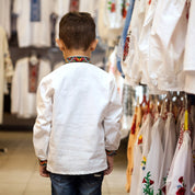 Boy wearing embroidered Vyshyvanka linen shirt in shop, showcasing Ukrainian folk style design.