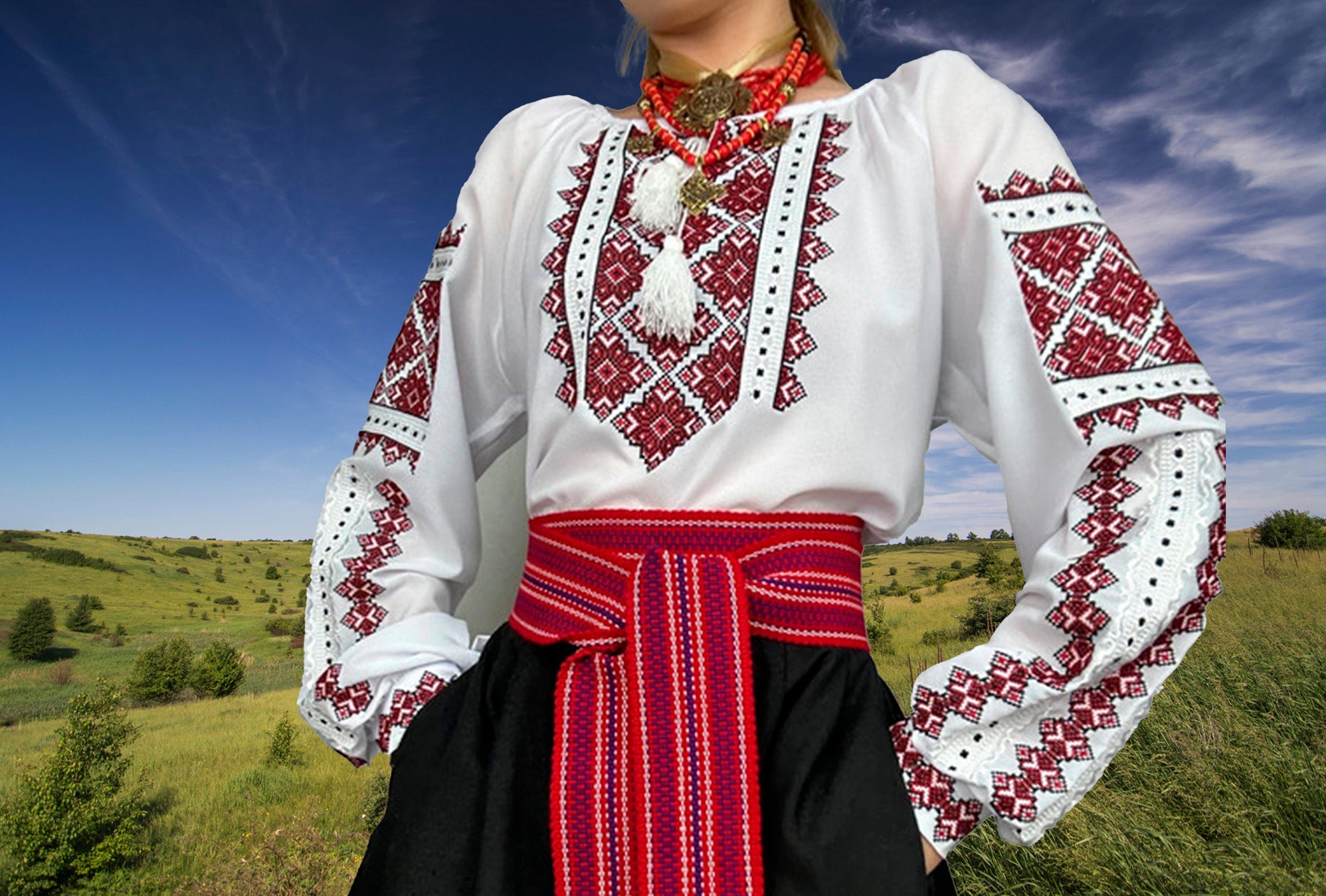 Traditional Ukrainian Vyshyvanka blouse with red cross-stitch embroidery, worn outdoors with a scenic background.