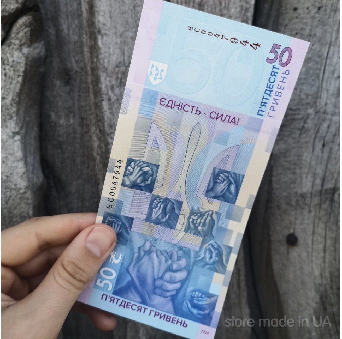 Limited edition Ukraine 50 UAH banknote "Unity Saves the World" held against a wooden background