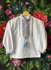Ukrainian boy vyshyvanka shirt with Tryzub embroidery, white sorochka with blue and yellow design on floral background.