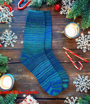 Blue-green hand knitted wool socks on wooden table with candles, candy canes, and snowflake decorations.
