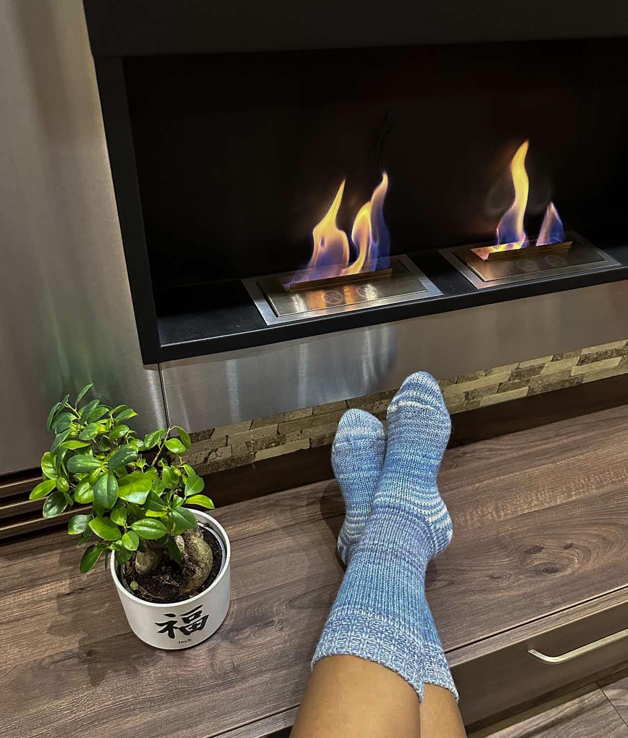 Cozy feet in wool socks relaxing by the fireplace, next to a potted plant. Perfect for warmth and comfort during winter.