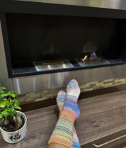 Cozy feet in colorful wool socks relaxing by a modern fireplace with a potted plant, showcasing warmth and comfort.