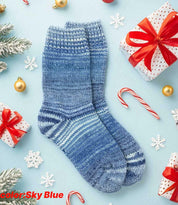 Sky blue hand knitted wool socks surrounded by festive Christmas gifts and decorations on a winter-themed background.