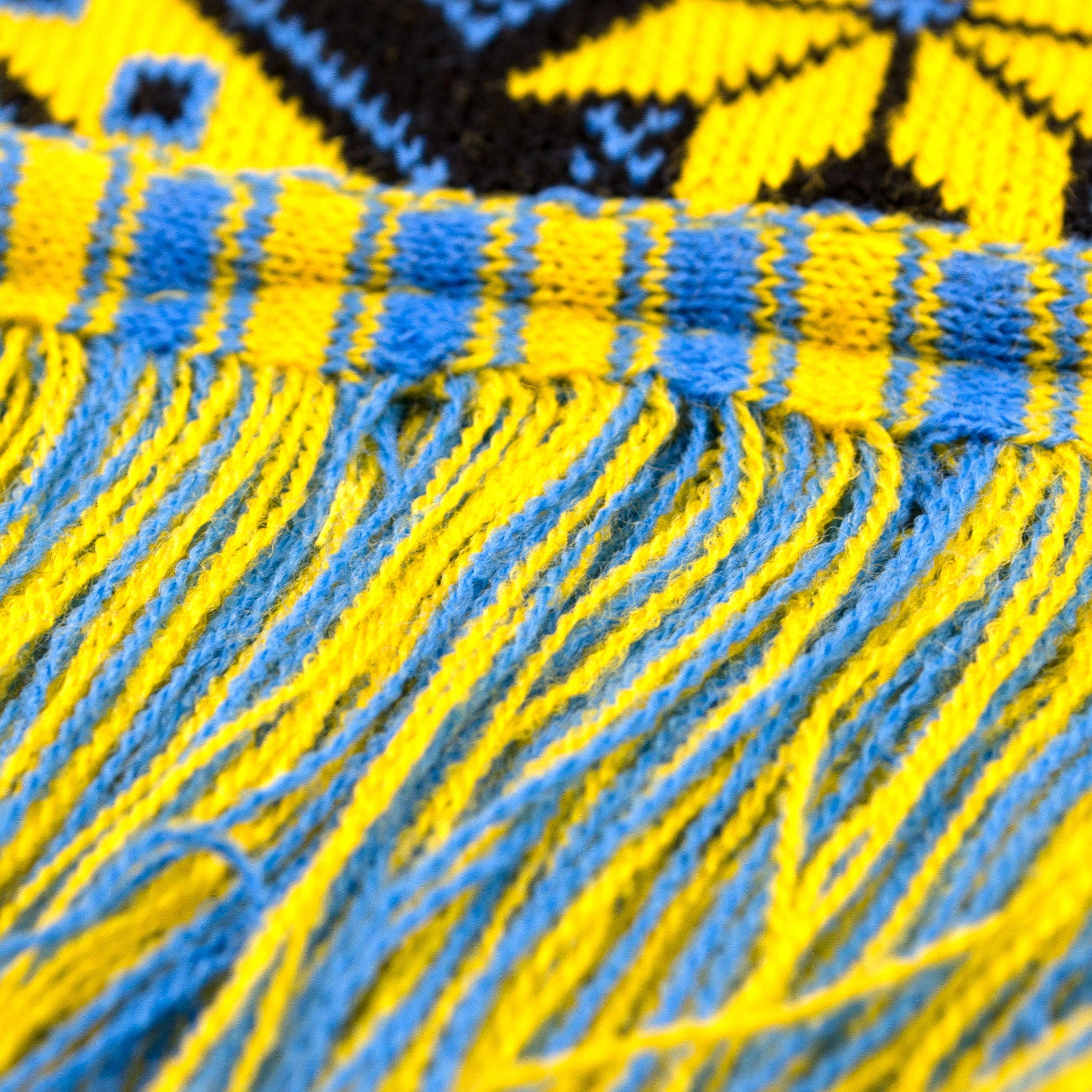 Cozy knit scarf with yellow-blue traditional geometric pattern and fringe detail, inspired by Ukrainian artistry.