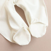 Close-up of a white baby romper with snap buttons, featuring soft footed design for comfort.