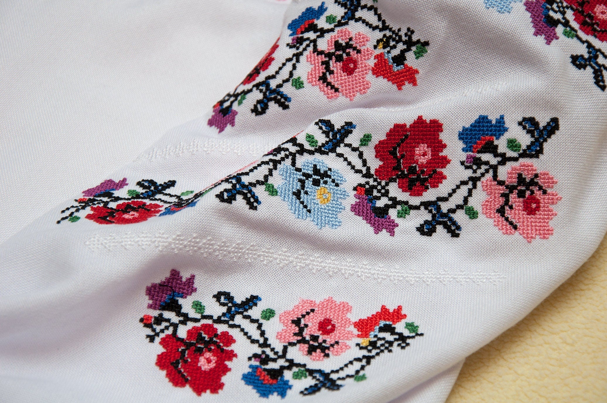 Close-up of Ukrainian embroidered floral blouse with colorful cross-stitch design, traditional Vyshyvanka style for girls.