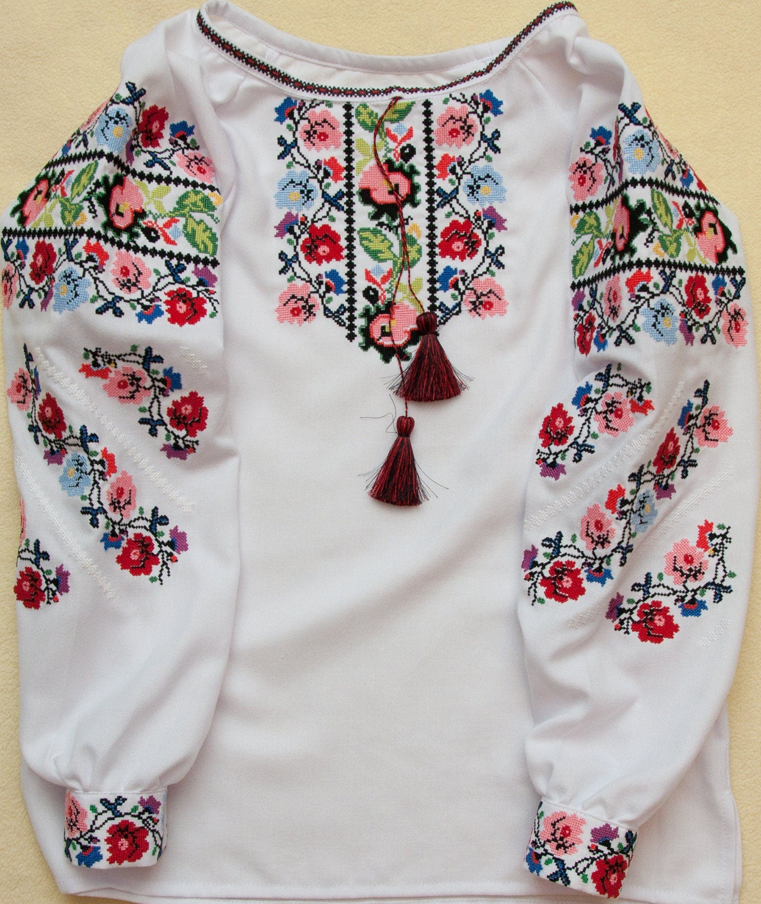 Traditional Ukrainian embroidered blouse for girls with vibrant floral design and colorful cross-stitch on white fabric.