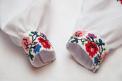 Close-up of Ukrainian embroidered blouse sleeves with colorful floral cross-stitch pattern for girls.