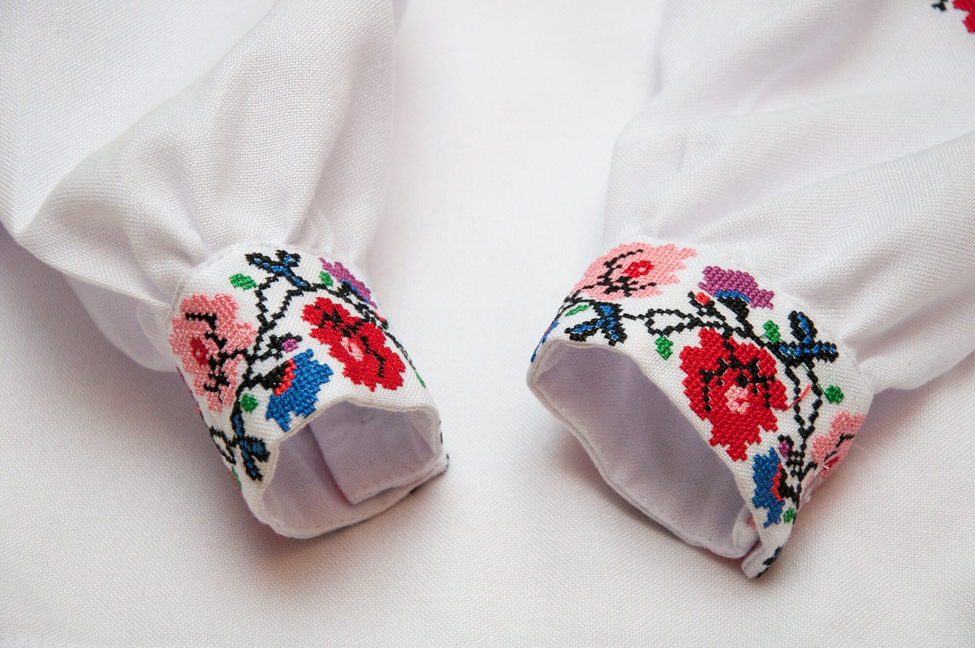 Close-up of Ukrainian embroidered blouse sleeves with colorful floral cross-stitch pattern for girls.