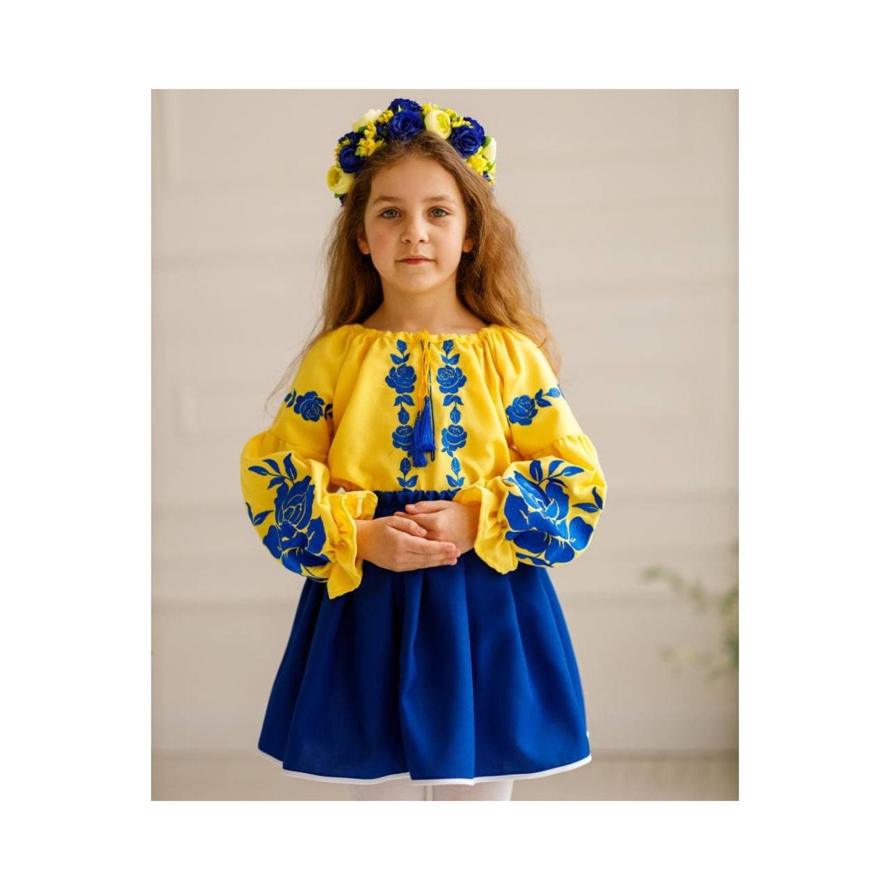 Girl wearing Ukrainian embroidered blouse and skirt set in blue and yellow, traditional folk outfit for cultural celebrations.