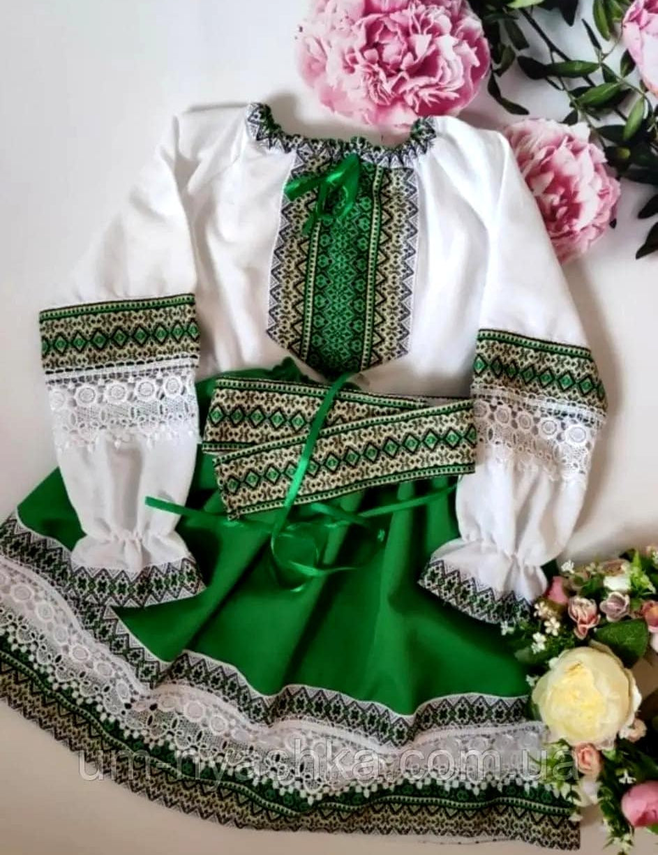 Green and white Ukrainian embroidered blouse and skirt set for girls, traditional folk-style outfit displayed with flowers.