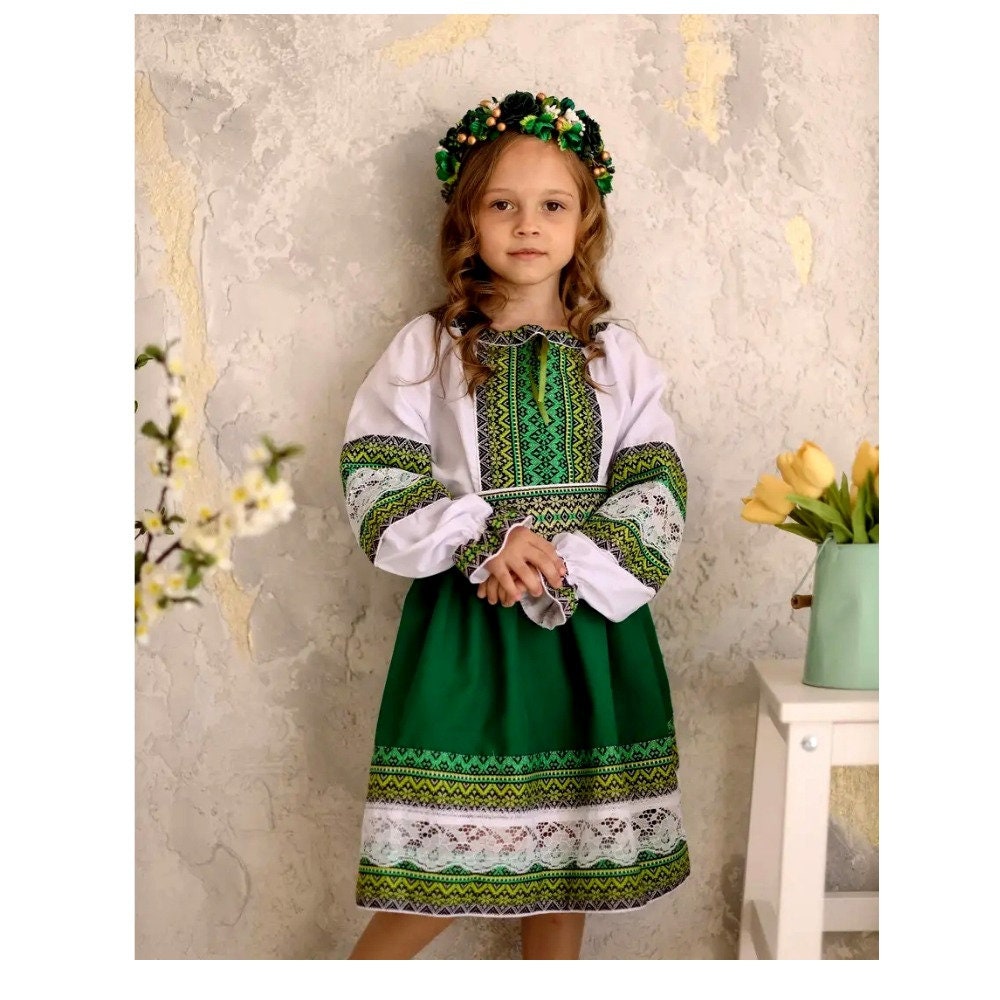 Girl wearing a green and white Ukrainian embroidered blouse and skirt set with floral accents, ideal for cultural events or celebrations.