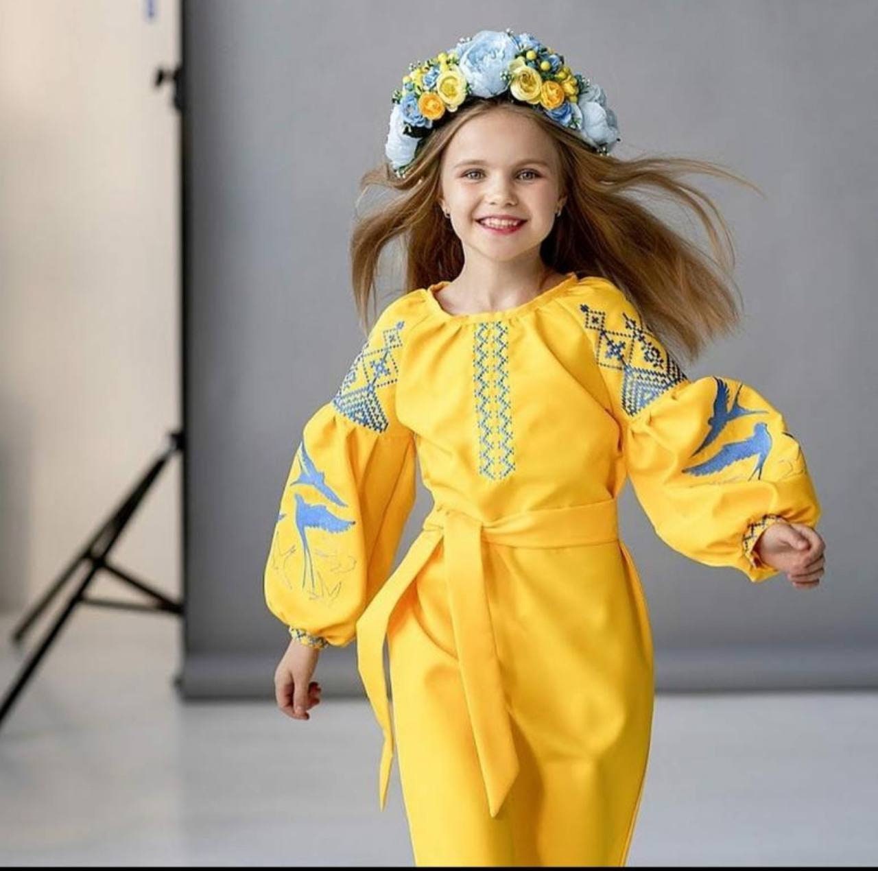 Girl in yellow Ukrainian embroidered dress with blue swallow motifs, celebrating tradition and culture.