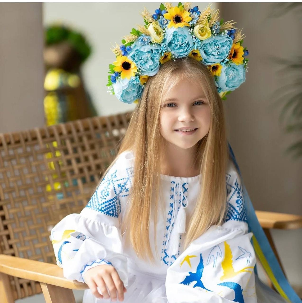 Girl wearing traditional Ukrainian embroidered dress with blue and yellow swallow motifs and floral headpiece, symbolizing heritage and culture.
