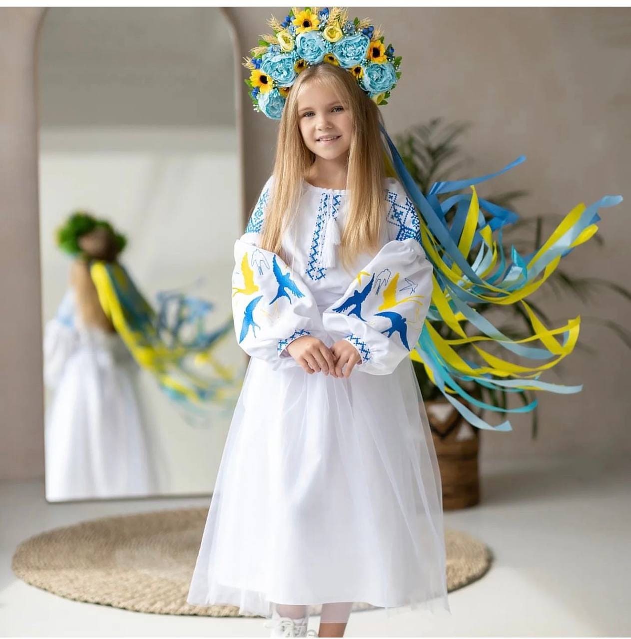 Girl wearing Ukrainian embroidered dress with blue and yellow swallow motif, symbolizing cultural heritage, in a festive setting.