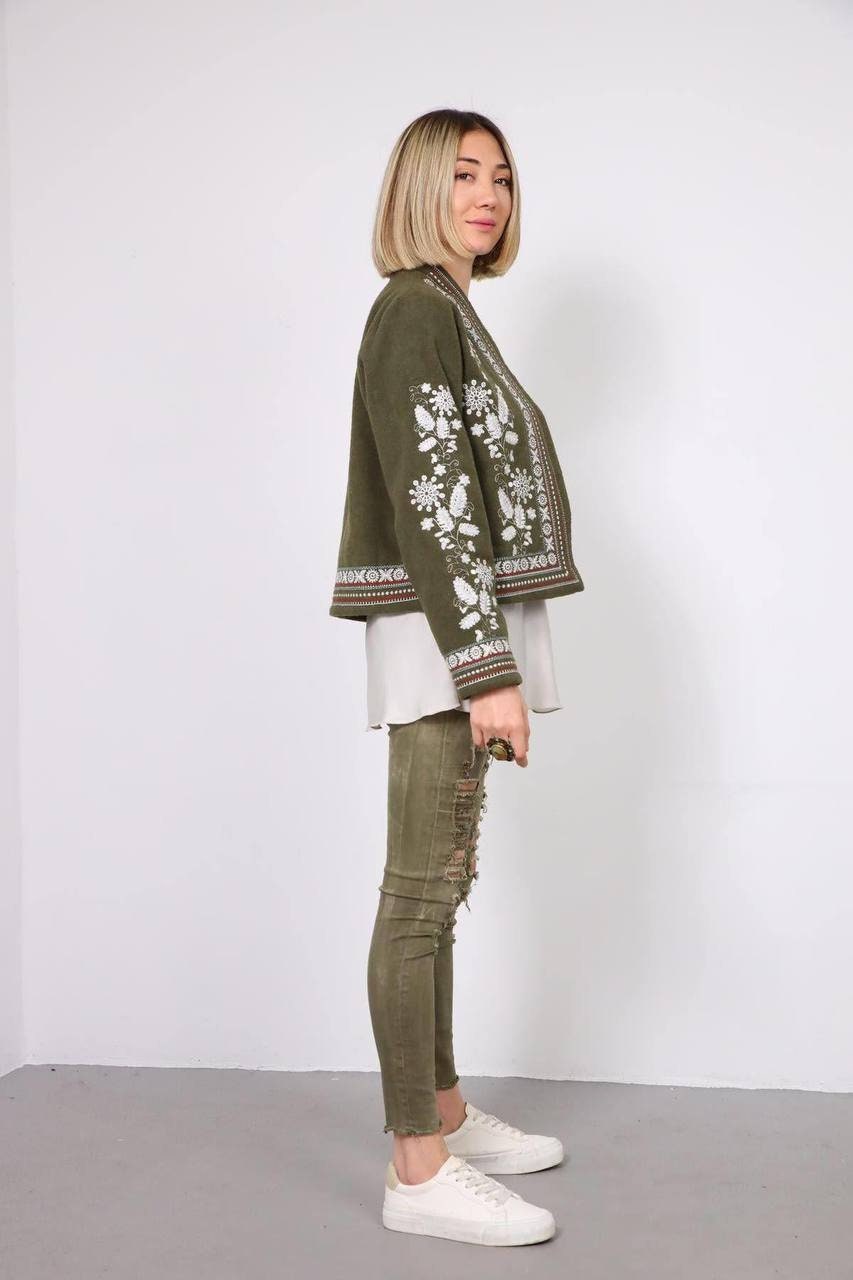 Woman wearing khaki Vyshyvanka style embroidered jacket with Ukrainian ornament, showcasing traditional elegance.