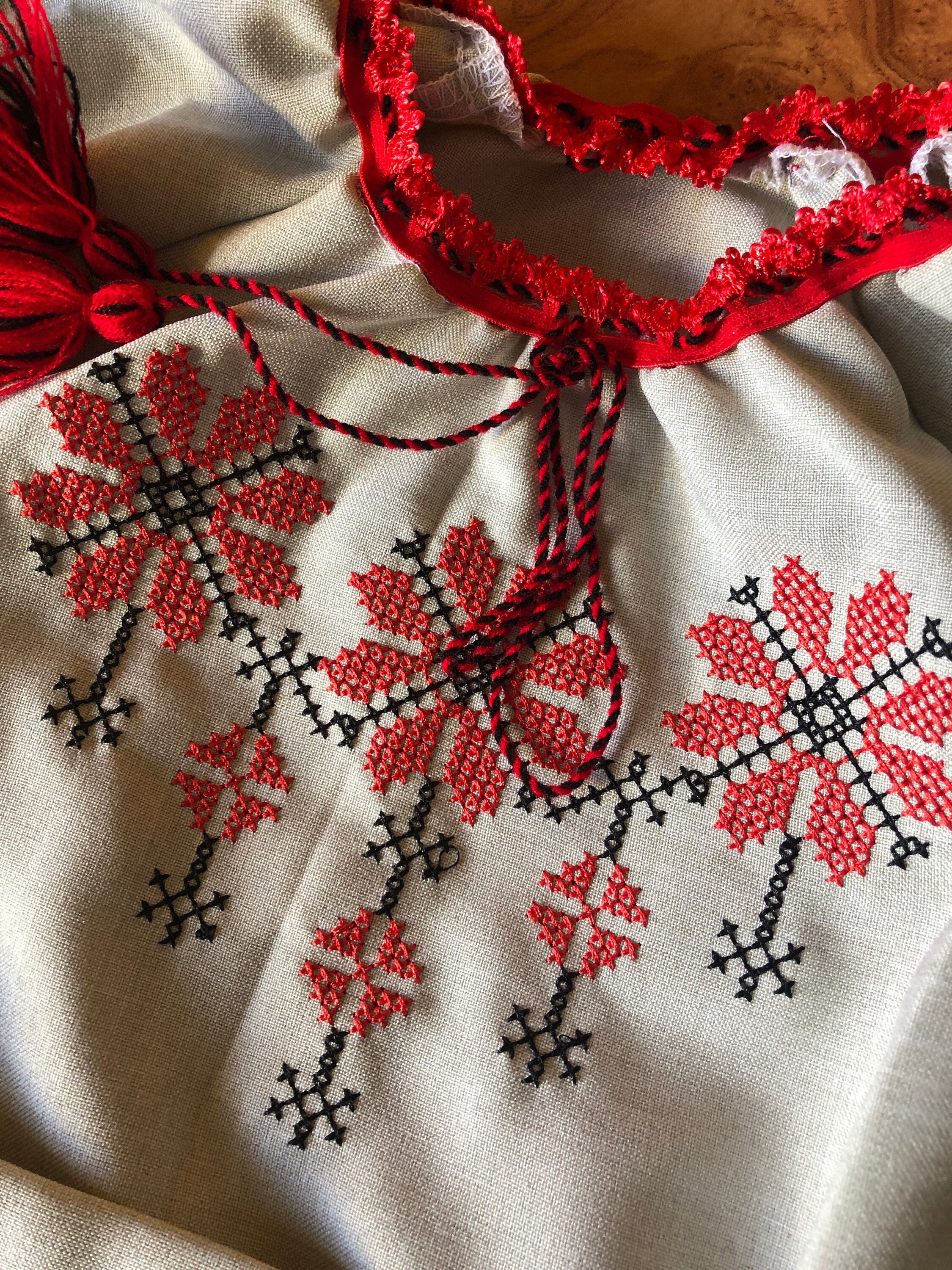 Close-up of Ukrainian embroidered linen dress with red floral Rosava motif, showcasing intricate traditional Vyshyvanka design.