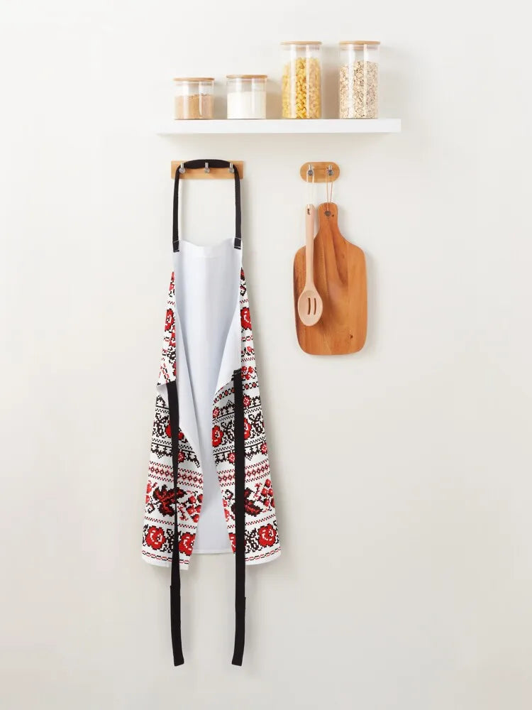 Ukrainian embroidered apron with red and black pattern hanging in a kitchen setting with culinary tools and spices on a shelf.