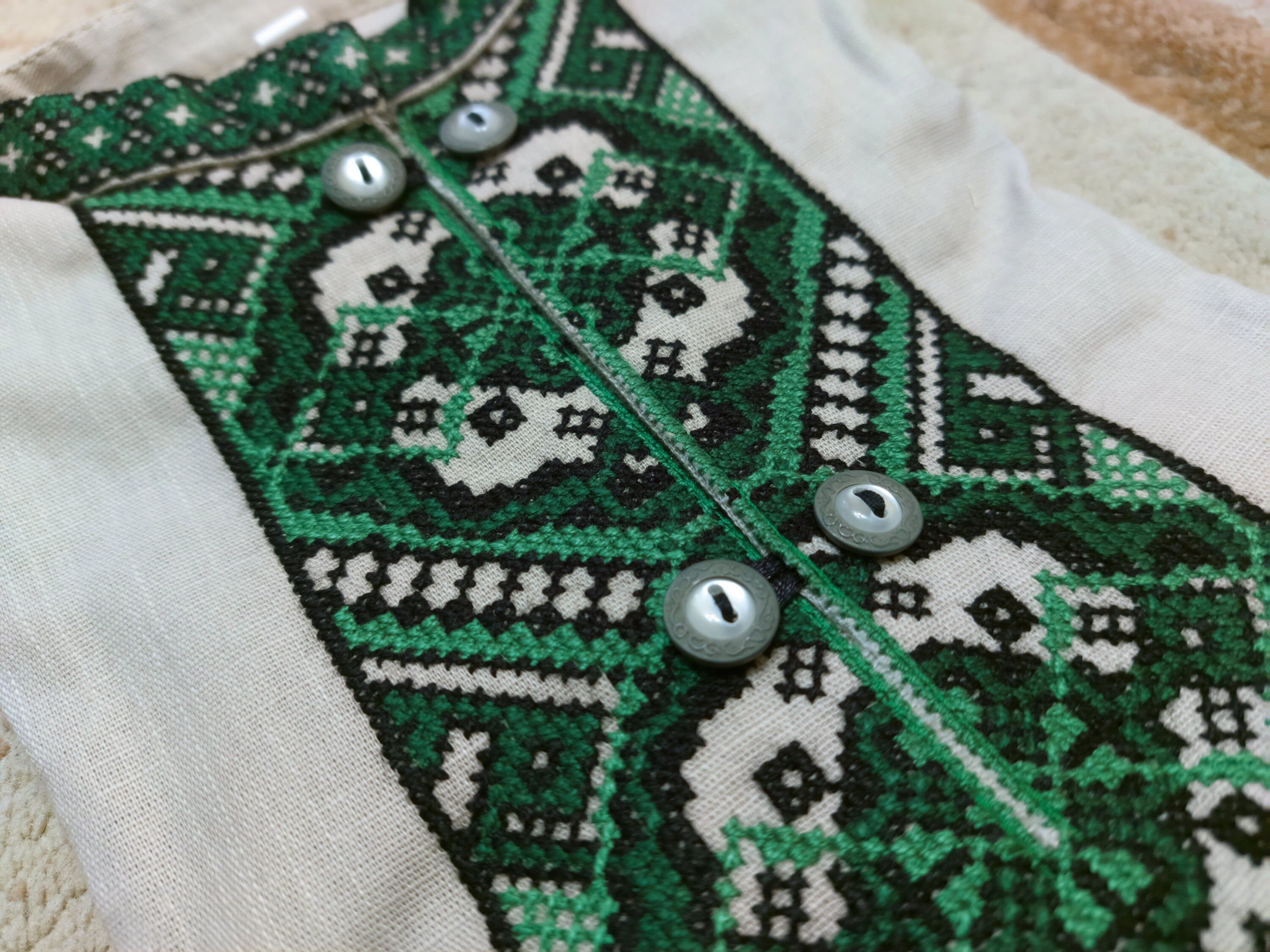 Traditional Ukrainian embroidered shirt for boys with green cross-stitch pattern and buttons, made from natural linen fabric.
