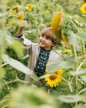 Boy wearing Ukrainian embroidered shirt in sunflower field, traditional vyshyvanka with green cross-stitch patterns, cultural attire for children.