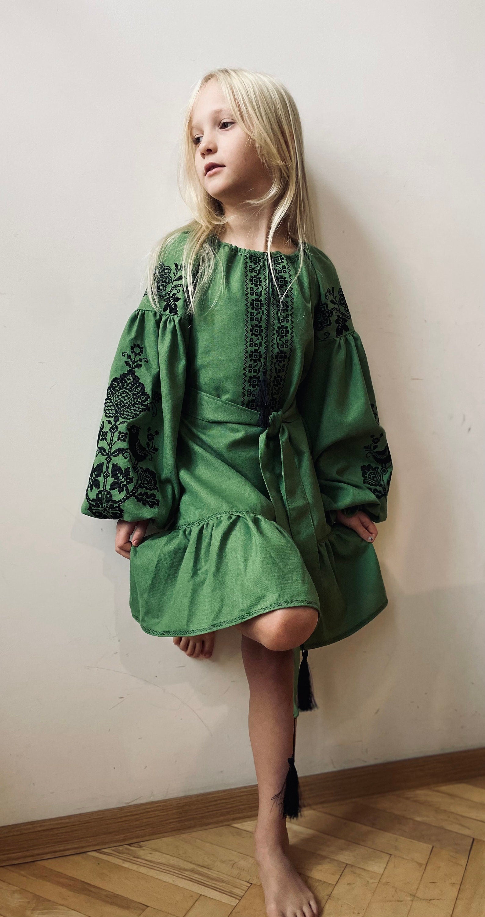 Girl wearing Ukrainian embroidered dress in traditional green Vyshyvanka style with cross-stitch details and silk threads.