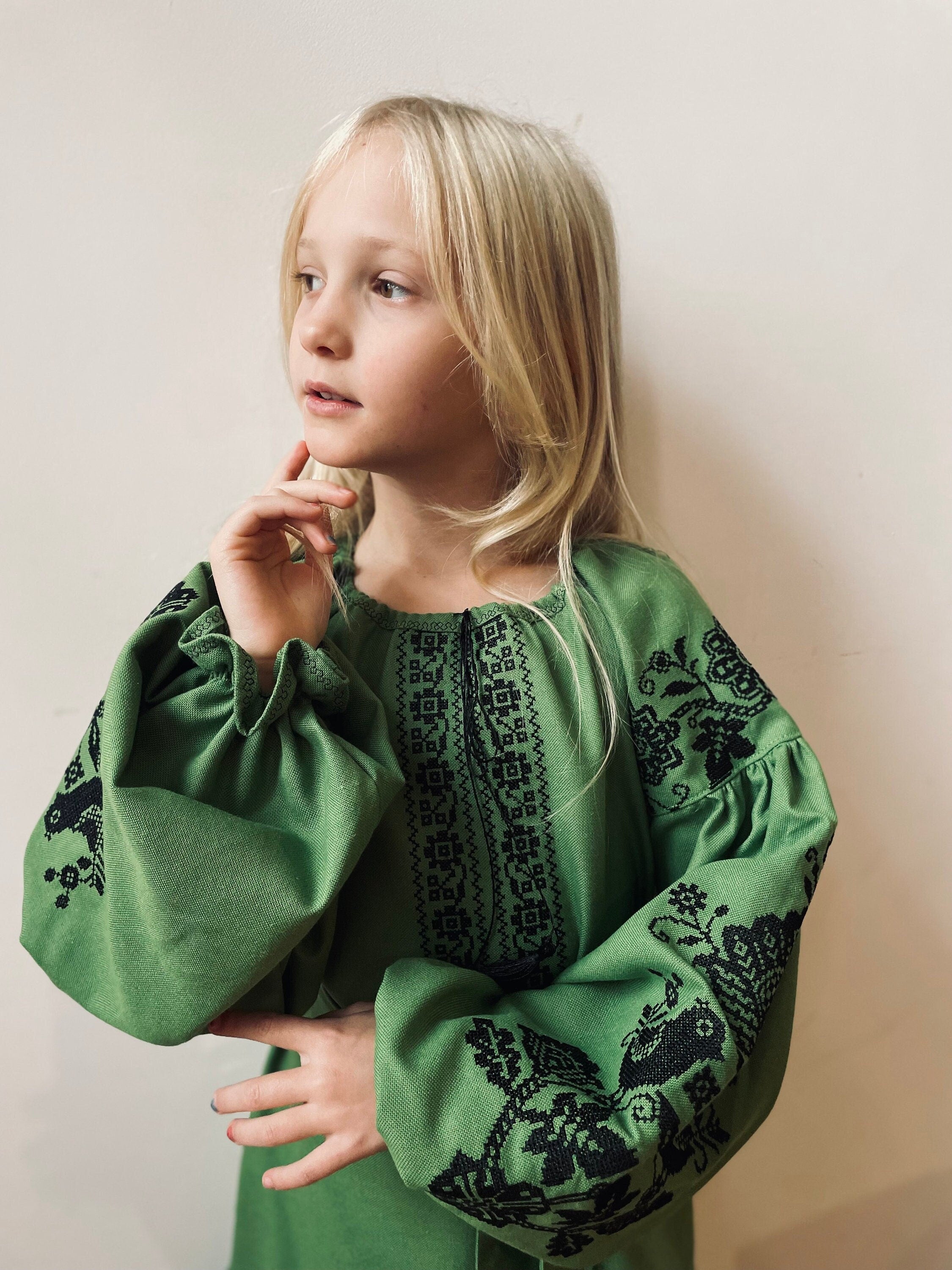 Girl in traditional Ukrainian Vyshyvanka dress with green fabric and black embroidery, showcasing boho style and cultural elegance.