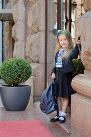 Young girl wearing a traditional Ukrainian embroidered shirt and black skirt, standing with a backpack, ready for a school event.