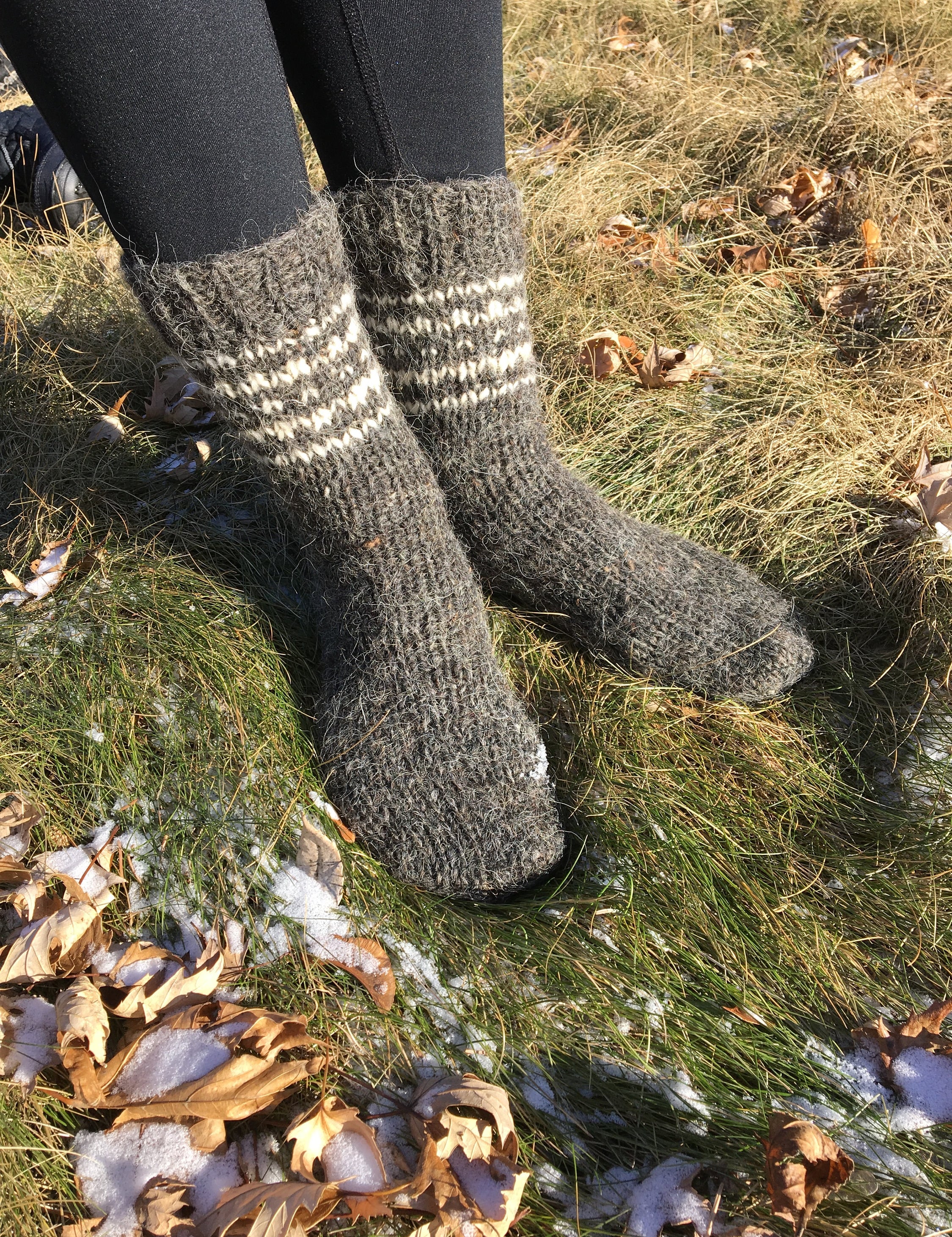 Unisex hand-knitted wool socks in grey, made from pure sheep wool, worn outdoors on grass in winter.